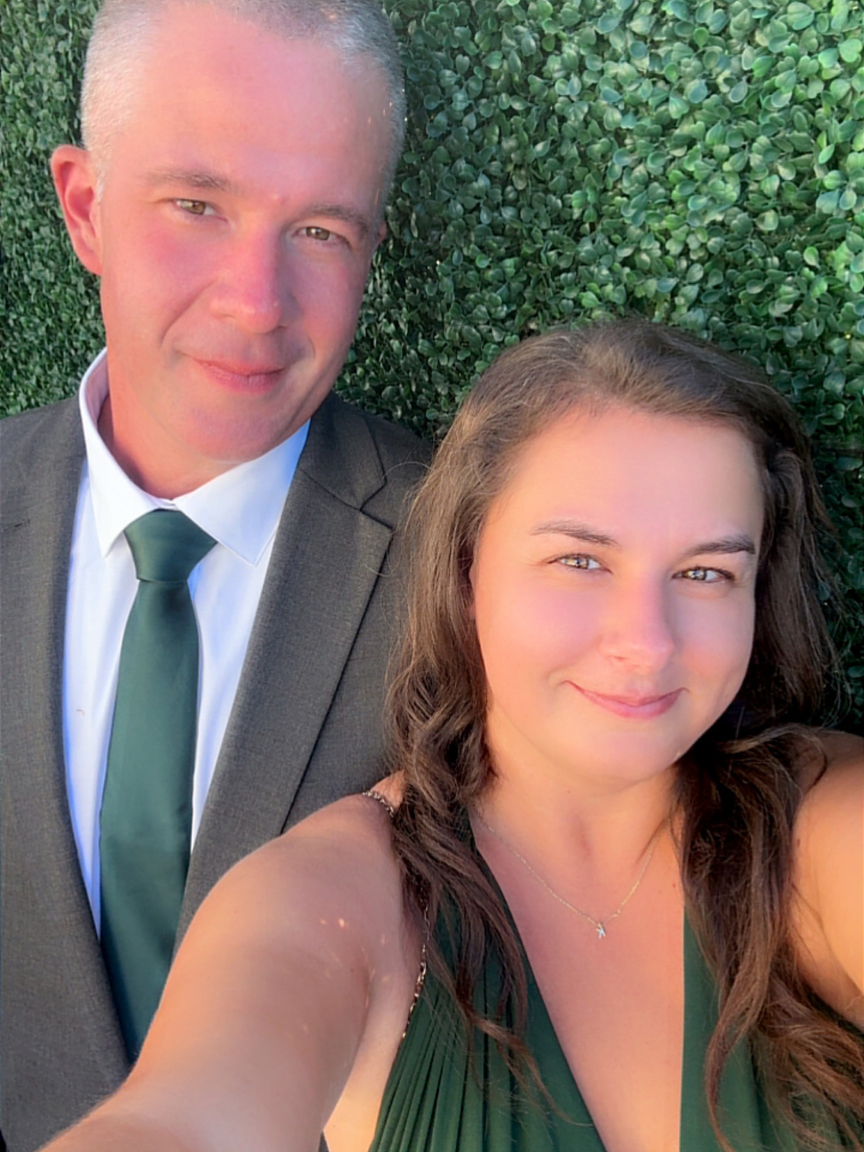 Katrina and Michael dressed up in front of a greenery wall
